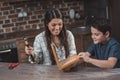 Little son and his smiling mother crafting a wooden birdhouse in kitchen