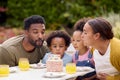 Family Celebrating Child\'s Birthday In Garden At Home Blowing Out Candles On Cake Royalty Free Stock Photo