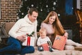 Family celebratory Christmas evening. Family three Caucasian people sitting under coniferous tree Christmas tree on floor of carpe