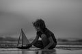 Family childhood concept. Kid boy holding tou boat. Cute little blond boy put toy boat in the sea water waves at the Royalty Free Stock Photo