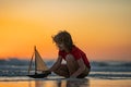 Family childhood concept. Kid boy holding tou boat. Cute little blond boy put toy boat in the sea water waves at the Royalty Free Stock Photo