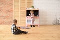 Family and children concept. Toddler boy playing on floor and cute little girl eating sweets at play kitchen in big empty room Royalty Free Stock Photo