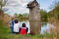 Family with children, feeding ducks in a river in front of old wooden cottage on brick pillar in The Radbuza River, near Chotesov Royalty Free Stock Photo