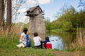 Family with children, feeding ducks in a river in front of old wooden cottage on brick pillar in The Radbuza River, near Chotesov Royalty Free Stock Photo