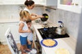 Family, children, hapiness and people concept. Happy family with children preparing pancakes in the kitchen. daughter helps