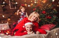 Family in Christmas Santa hats lying on bed. Mother, father and baby having fun in living room decorated by Christmas tree and Royalty Free Stock Photo