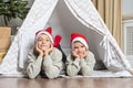 Two brothers in a Santa hat, lying in a children& x27;s tent in the room, impatiently waiting for Christmas and gifts.
