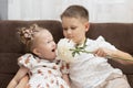 Family concept. Brother and sister play happily in home interior. A boy gives a delicate white flower to a little