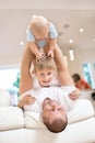 Family concept, father playing on sofa with baby and his brother, happy childhood. Indoor shot in the kitchen. a baby in her arms Royalty Free Stock Photo