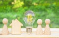 Family concept. Wooden house, lightbulb and many little men on a wooden table. Energy saving, debts for utility bills. Copy space Royalty Free Stock Photo