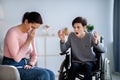 Family conflict concept. Sad mother crying and her disabled teenage son in wheelchair shouting at her, indoors Royalty Free Stock Photo