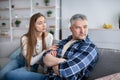 Family conflict concept. Upset mature man sitting on couch, his wife trying to make peace after fight at home Royalty Free Stock Photo