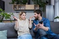 Family conflict at home. An angry man suspects a woman of treason, shouts at her, demands explanations, shows the phone, messages Royalty Free Stock Photo