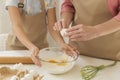 Family cooking. Maure lady adding egg to flour while little girl helping her in kitchen, closeup