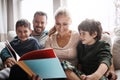 Family, couple and children on sofa for storytelling time with books and learning in family home. Love, reading and