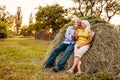 Family couple of farmers sitting on haystack and relaxing at sunset in countryside. Hard-working people hugging Royalty Free Stock Photo