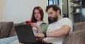 Family couple uses a laptop computer and smartphone, while relaxing on couch of their apartment in the living room. Man