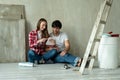 Family couple using digital tablet during renovation in new house. Young couple sits on the floor and using a tablet in