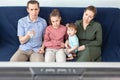 Family with dad, mom, teen daughter and infant child watching tv-set while sitting on sofa in a domestic room, staying at home Royalty Free Stock Photo