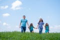 Family dad, mom and two children walk on green grass against blue sky. Happy caucasian parents with two daughters Royalty Free Stock Photo