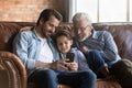 Retired grandpa young father preteen boy relax indoors use smartphone Royalty Free Stock Photo