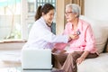 Family doctor or nurse checking smiling senior patient using stethoscope during home visit,young female home caregiver,health