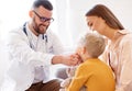 Family doctor pediatrician conducts examination of child boy with his mother, looks at his throat