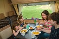 Family eating together in RV interior, parents and kids travel in motorhome camper, caravan on family vacation