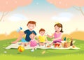 Family enjoying picnic. They are sitting on the grass in a park, the basket with meal and toys for the kids. Blurred background.