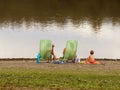 Family: father, mother and son are resting on beach chairs on the shore by the pond. Family holiday on the water. Beach of sand an