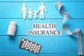 Family figure, pills, measuring tape and phrase Health insurance on wooden background Royalty Free Stock Photo