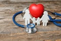 Family figure with stethoscope and heart on wooden background.