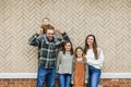 A family of five with two girls and a baby boy standing in front of a brick herringbone