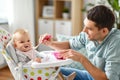 Father feeding happy baby in highchair at home Royalty Free Stock Photo