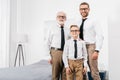 Father son and grandfather wearing formal clothing and glasses standing in bedroom and looking