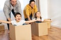 Family of four have fun in new house, parents riding kids in cardboard boxes Royalty Free Stock Photo