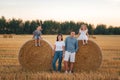 A family of four have rest near a haystack in a wheat field in summer at sunset time Royalty Free Stock Photo
