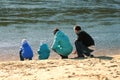 Family of four launches paper boats near the water. View from the back.