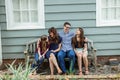 A family of four with a mother and father and two daughters sitting on a bench outside a blue cottage house