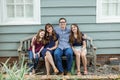 A family of four with a mother and father and two daughters sitting on a bench outside a blue cottage house