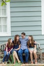 A family of four with a mother and father and two daughters sitting on a bench outside a blue cottage house Royalty Free Stock Photo