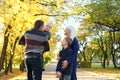 A family of four poses in an autumn park. The father holds the youngest son in his arms, the mother and elder brother