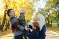 A family of four poses in an autumn park. The father holds the youngest son in his arms, the mother and older brother