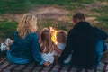 Family of four are sitting on a grass by the fire and watching the sunset with their backs Royalty Free Stock Photo