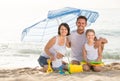 Family of four sitting together under beach umbrella on beach Royalty Free Stock Photo