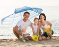 Family of four sitting together under beach umbrella on beach Royalty Free Stock Photo