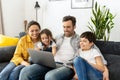 Family of four using laptop sitting on the sofa in cozy apartment, parents and two kids watching movie on computer Royalty Free Stock Photo