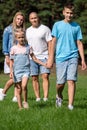 A family of four walks hand in hand through a sunny park, showcasing a moment of unity, bonding and peaceful coexistence