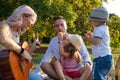 Family of four with young children in the park picnicking while mom plays guitar Royalty Free Stock Photo