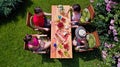 Family and friends eating together outdoors on summer garden party. Aerial view of table with food and drinks from above